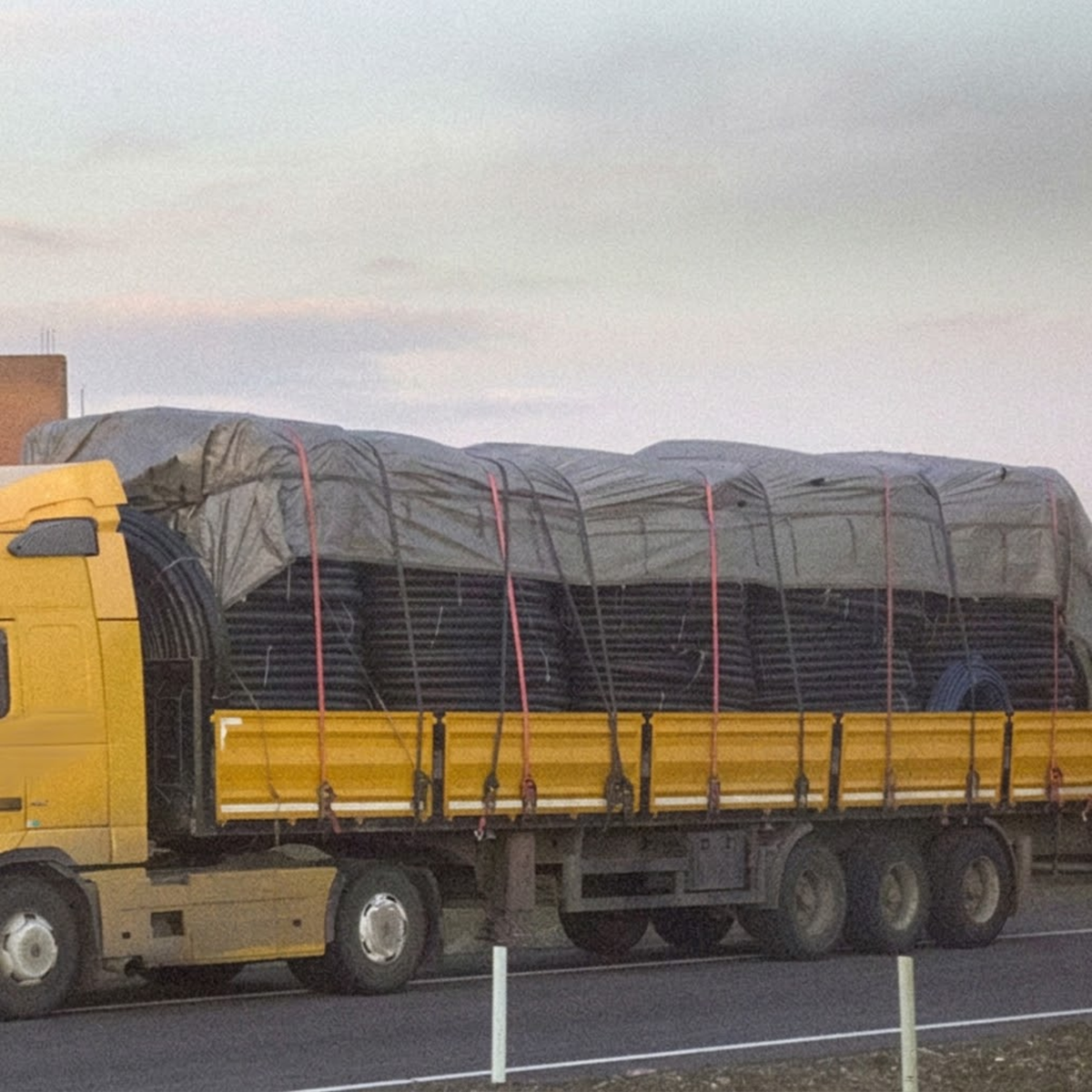 Ratchet tie down straps securing a tarpaulin-covered load on a yellow semi-trailer truck
