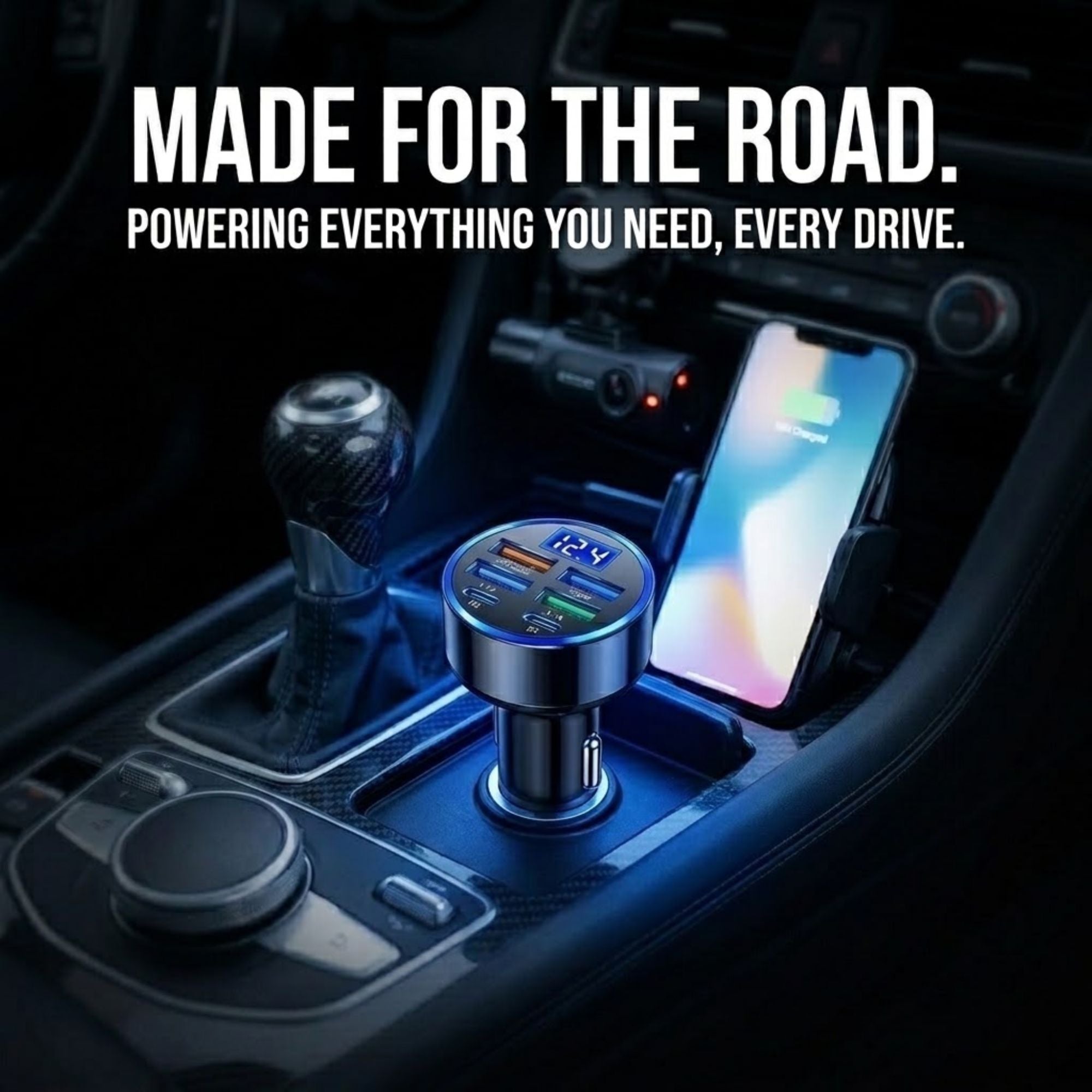 A car center console with a portable multi-port charger plugged into the console, next to a smartphone in a phone holder. Large white text at the top reads 'MADE FOR THE ROAD.