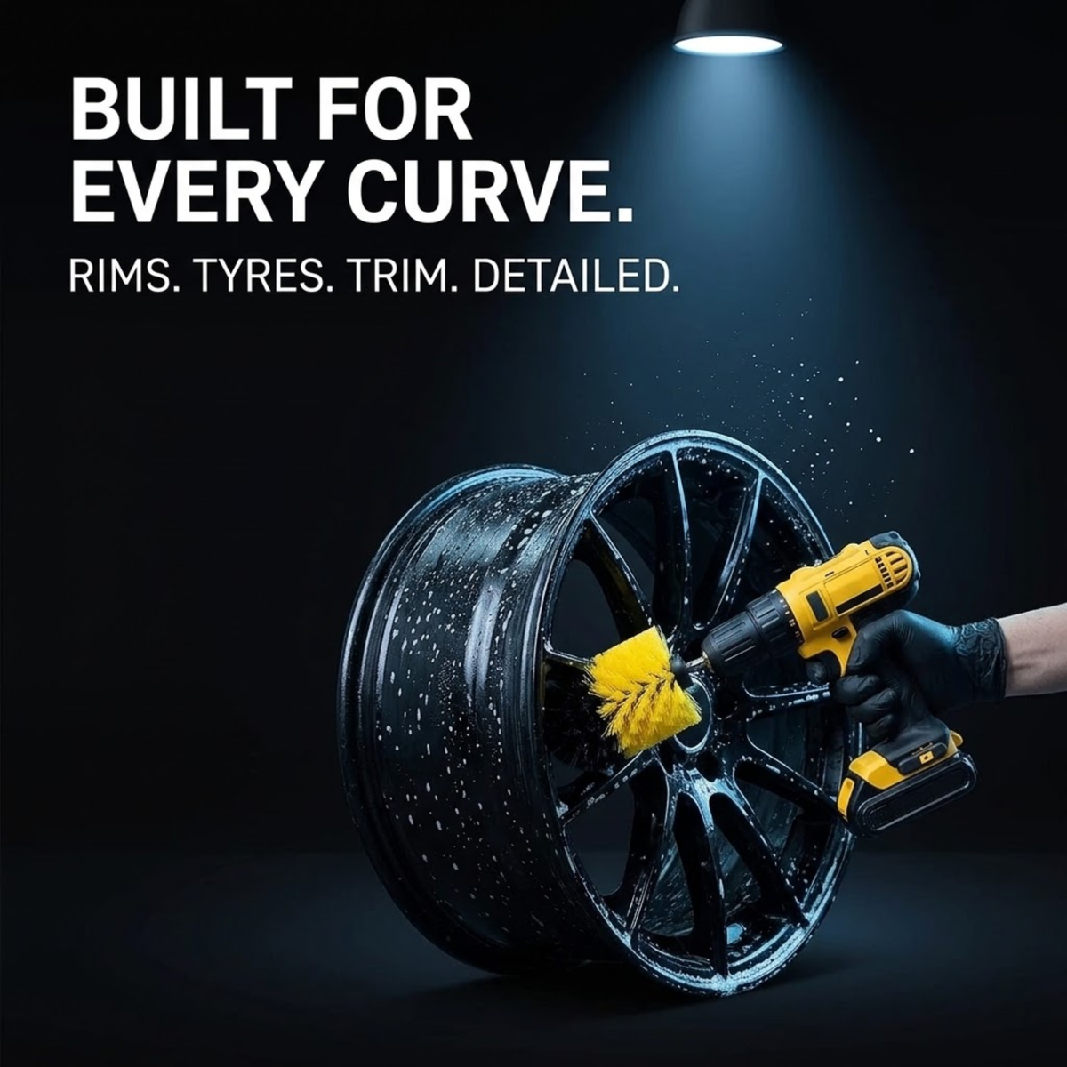 A black multi-spoke wheel rim being cleaned by a gloved hand holding a yellow cordless brush attachment. The scene is dark with dramatic spotlighting and white text reading 'BUILT FOR EVERY CURVE.