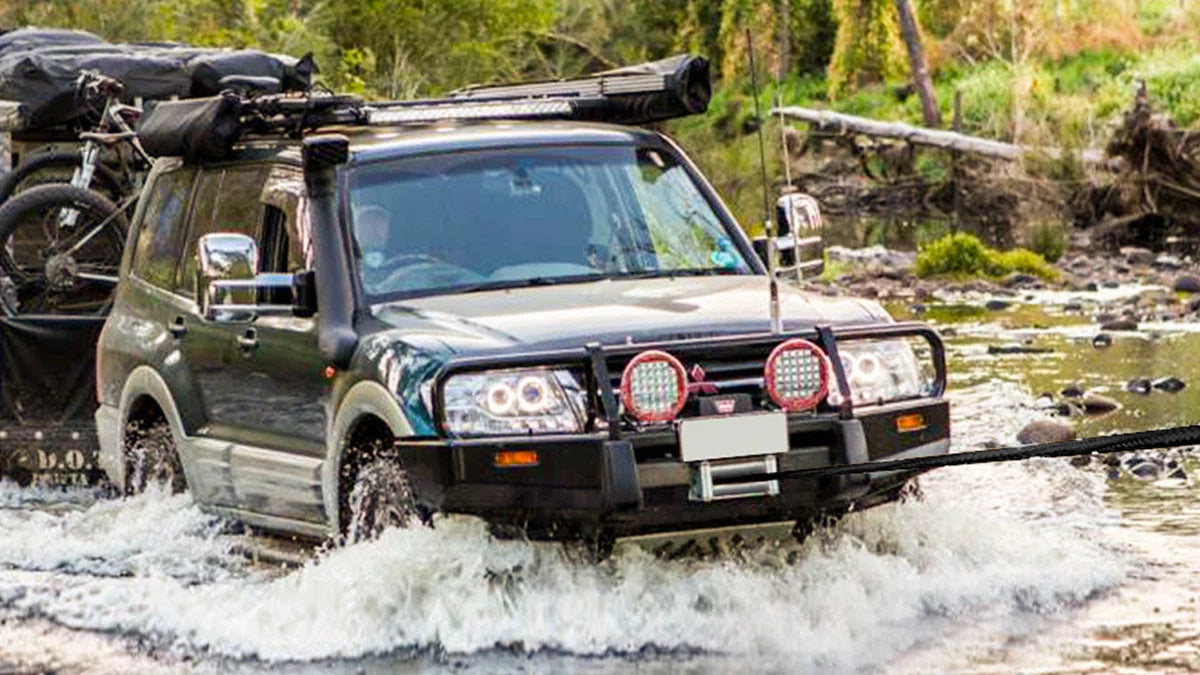 An off-road SUV driving through shallow water with a tow bar attached to a set of five colorful rope tow straps shown below on a white background.