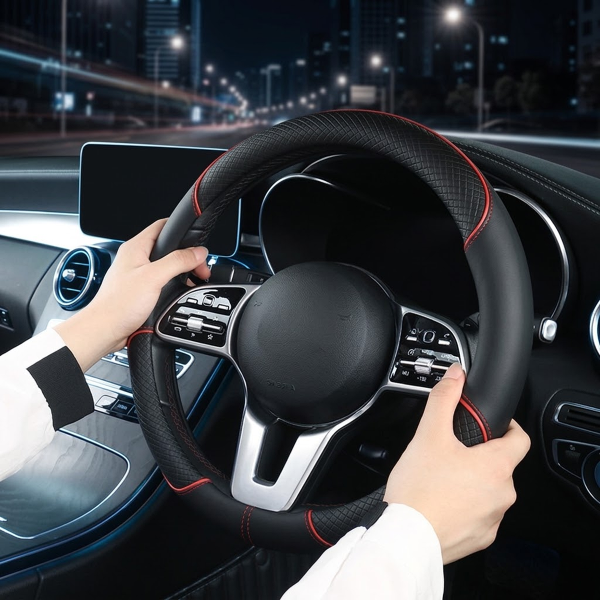 A close-up of a person's hands holding a black steering wheel with red stitching inside a car at night.