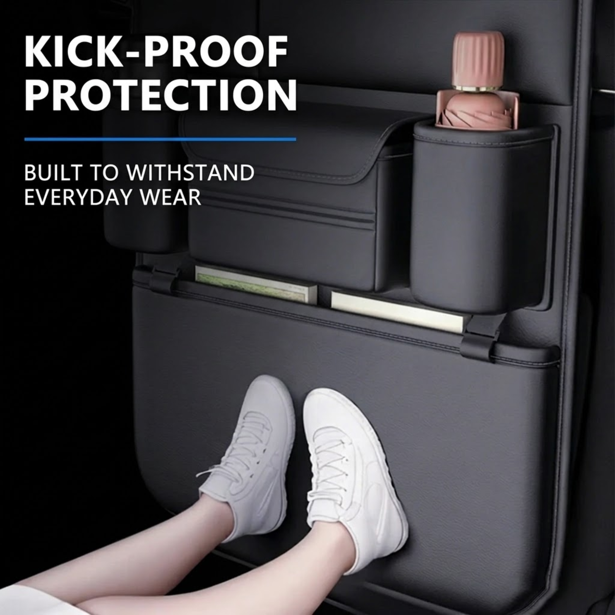 A dark gray kick-proof storage organizer mounted on a car seat, shown with a person's legs and white sneakers resting underneath to demonstrate use. The organizer features a cup holder with a pink bottle, a side pocket, and a lower storage compartment.