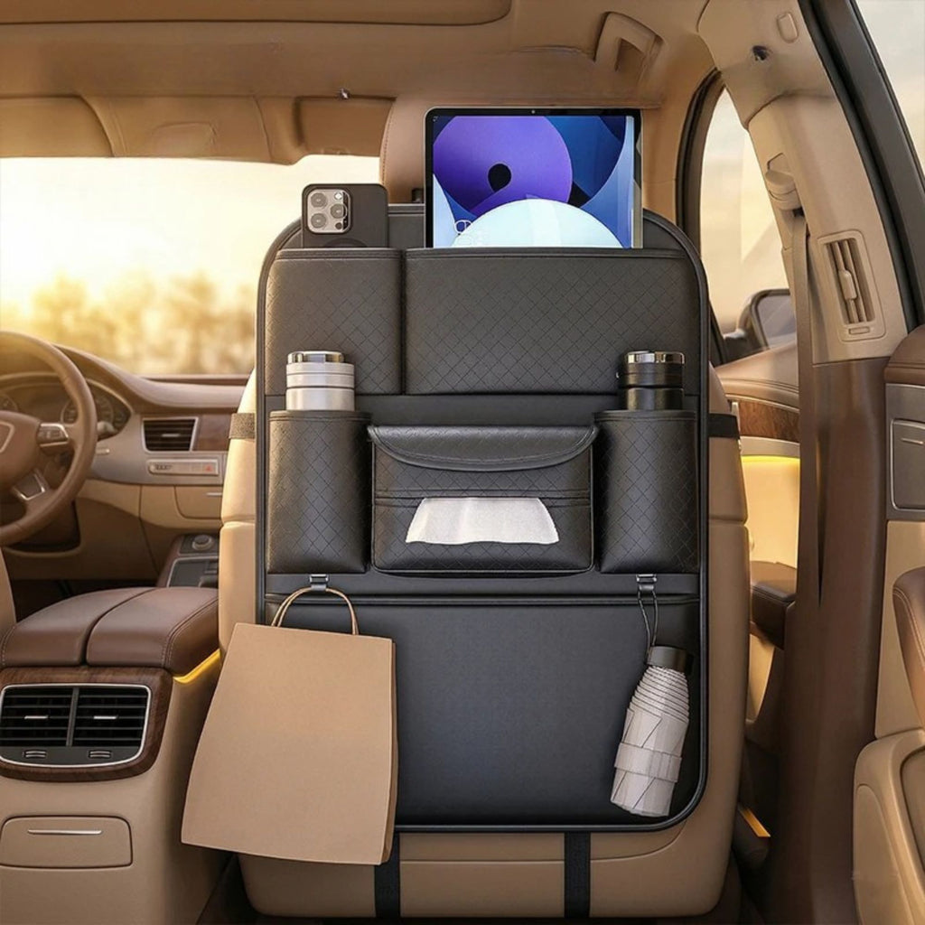 A black car rear-seat organizer hanging over the center console, shown inside a beige vehicle interior. The organizer has quilted pockets, a tissue slot, cup holders, a hanging bag loop, and a tablet mounted at the top.