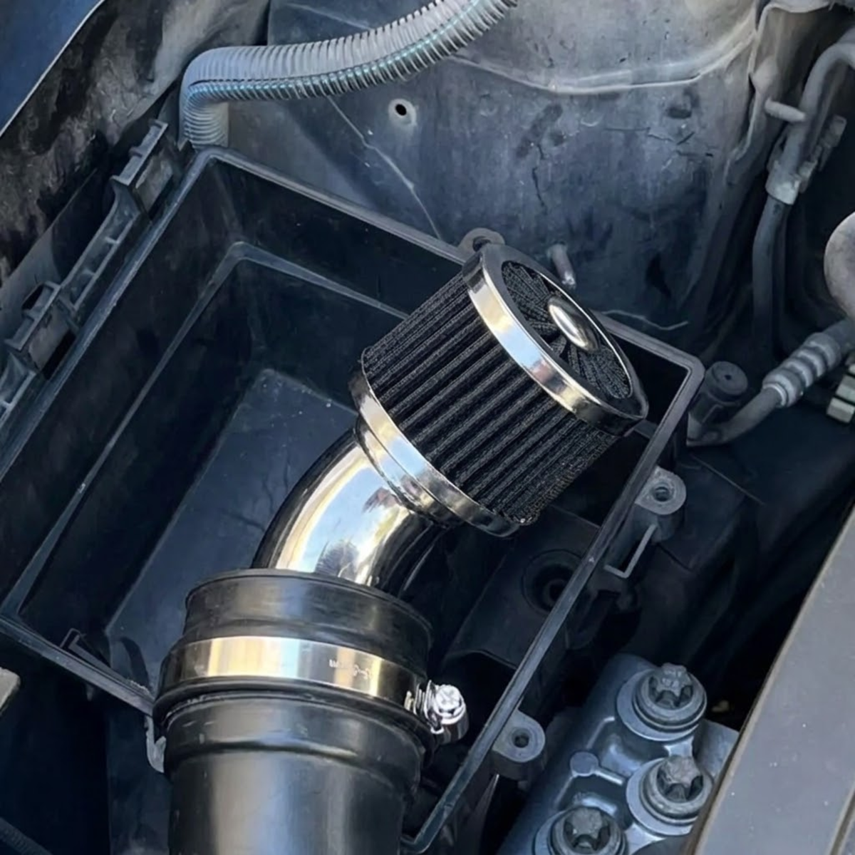 Chrome cone air breather filter fitted to a vehicle engine bay intake pipe, replacing the factory crankcase vent