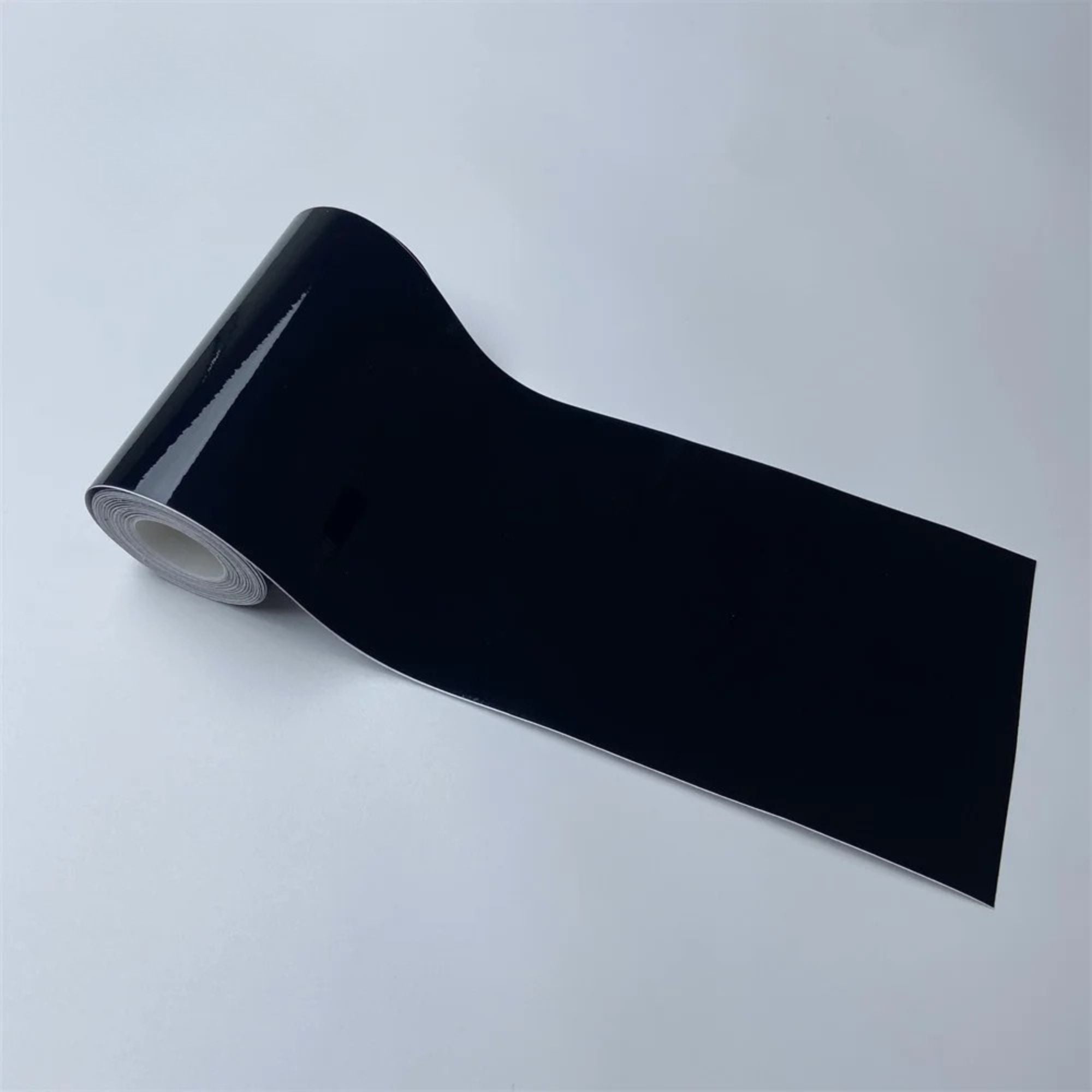 Roll of Gloss Black Trim Wrap vinyl film partially unrolled, close-up view on a white background