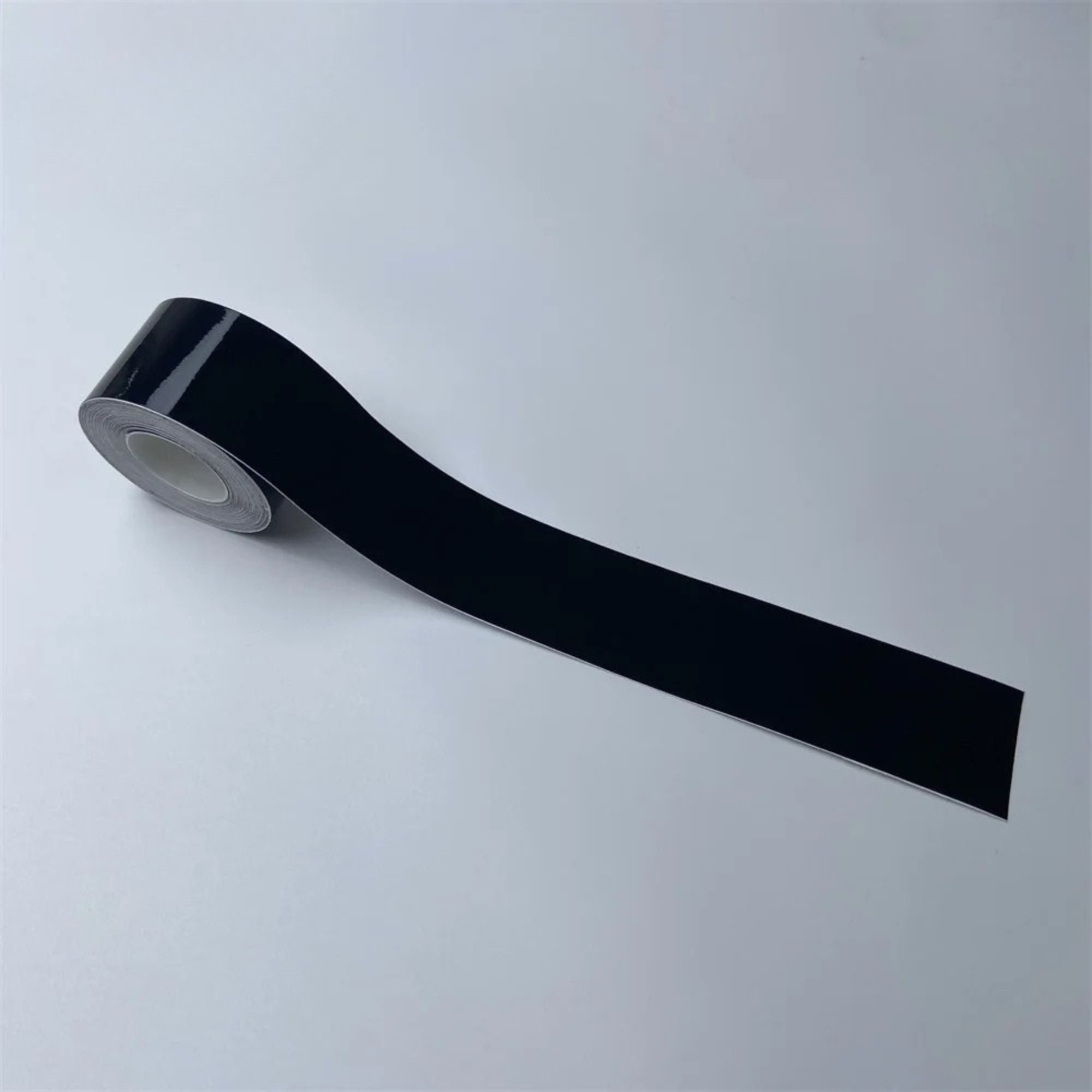 Roll of Gloss Black Trim Wrap vinyl film partially unrolled, angled view on a white background