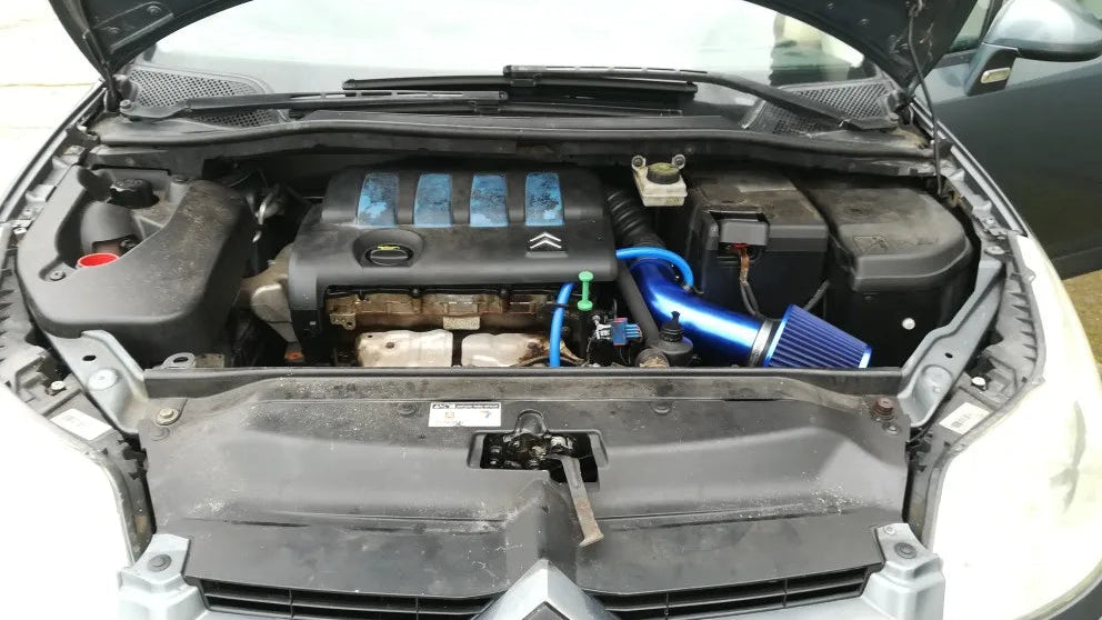 A blue air filter and intake tube installed on a black engine bay of a car with the hood open.