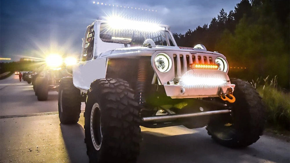 Off-road vehicle with large LED light bar on a road at night.