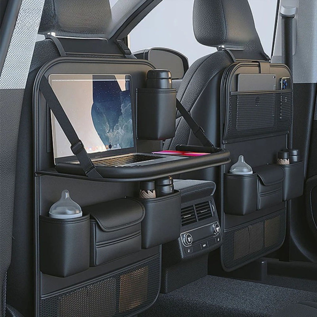 Black car backseat organizer panels mounted on the rear seats of a vehicle, featuring a folding tray table with a laptop, cup holders, storage pockets, and bottle holders.