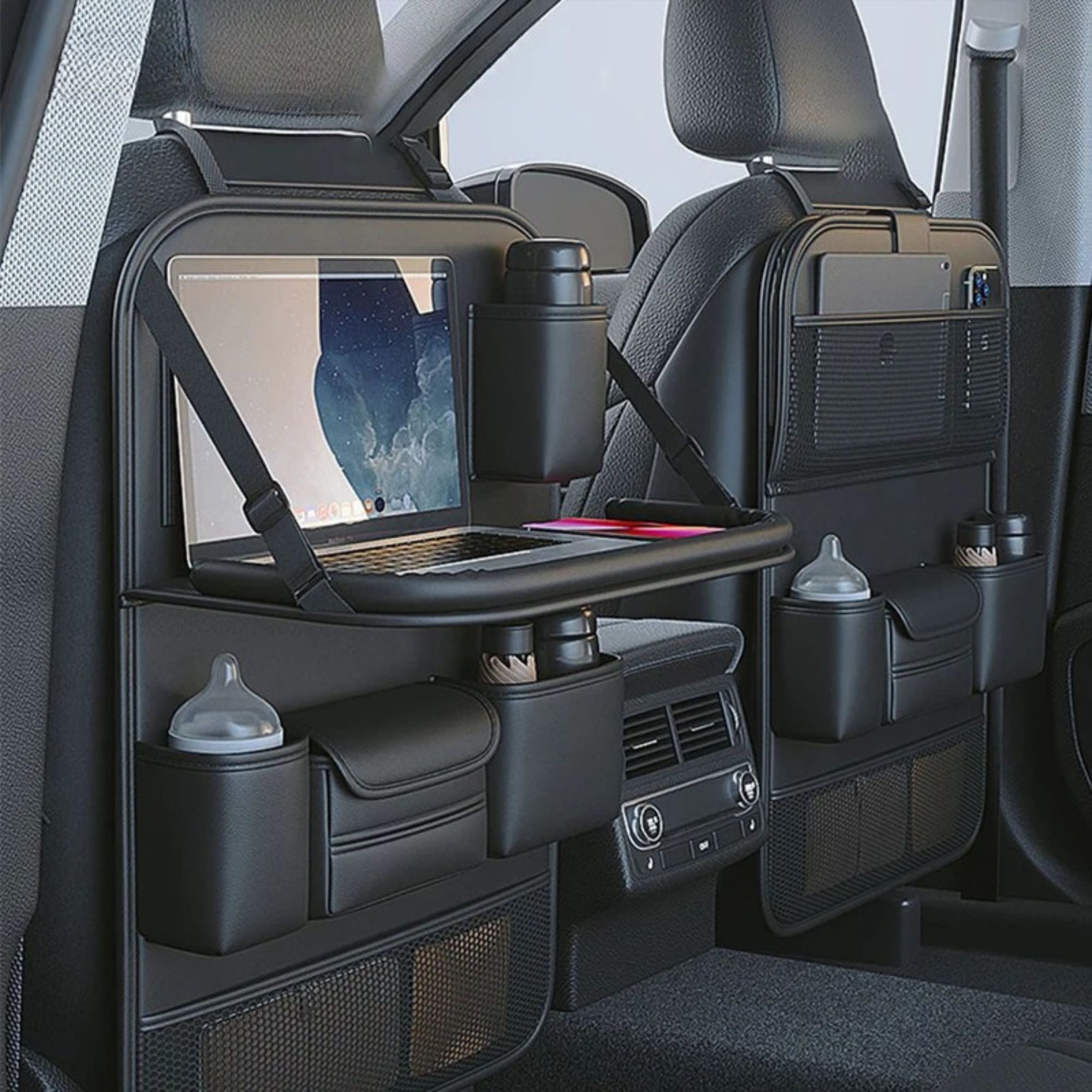 Black car backseat organizer panels mounted on the rear seats of a vehicle, featuring a folding tray table with a laptop, cup holders, storage pockets, and bottle holders.