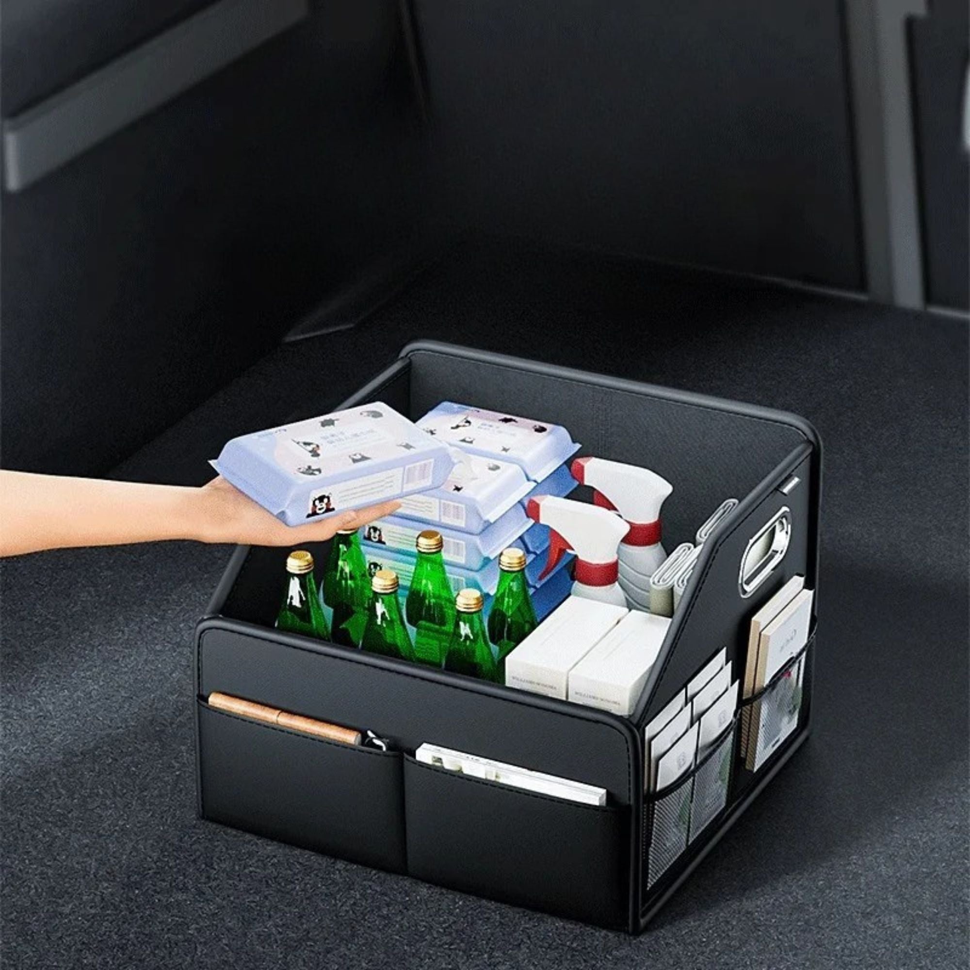 Hand placing items into a black leather car boot organiser filled with drink bottles inside a vehicle trunk