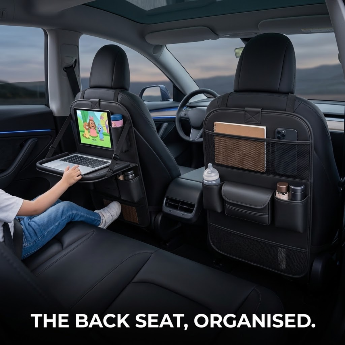 Leather backseat organiser fitted to two car seats, with a child using the fold-down tray and tablet holder in the rear seat