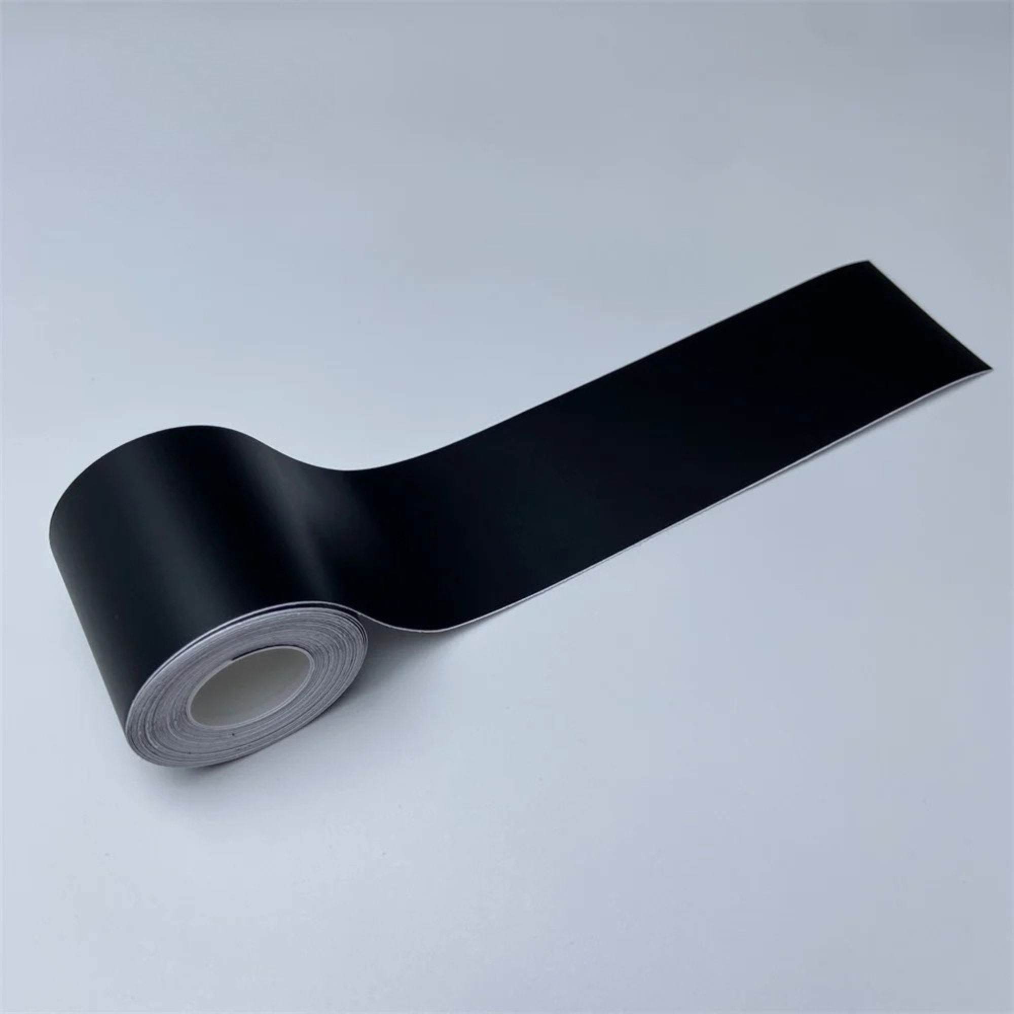 Roll of Matte Black Trim Wrap vinyl film partially unrolled, angled view on a white background