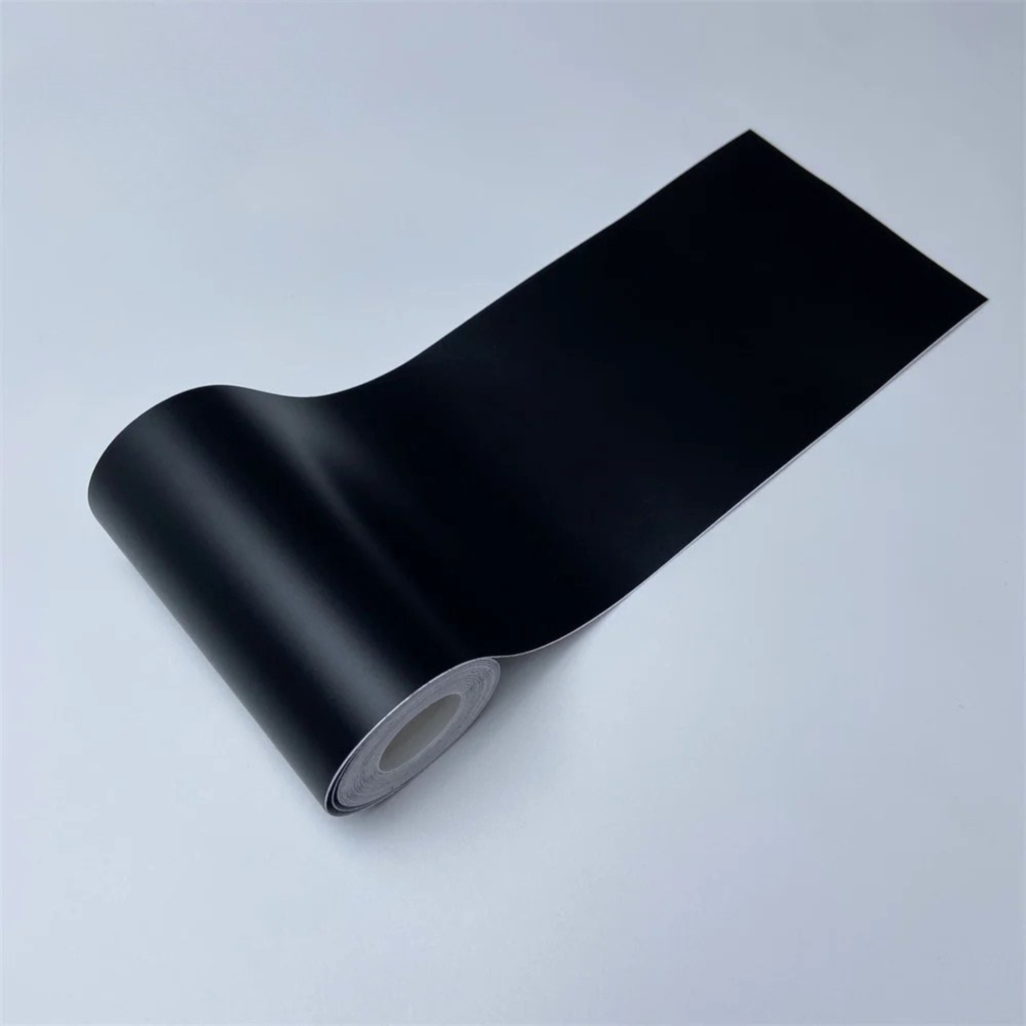 Roll of Matte Black Trim Wrap vinyl film partially unrolled, close-up view on a white background