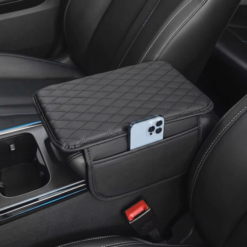 A black quilted car center console organizer tray mounted between front seats, shown holding a smartphone in its side pocket. The product is installed inside a car interior with black leather seats.