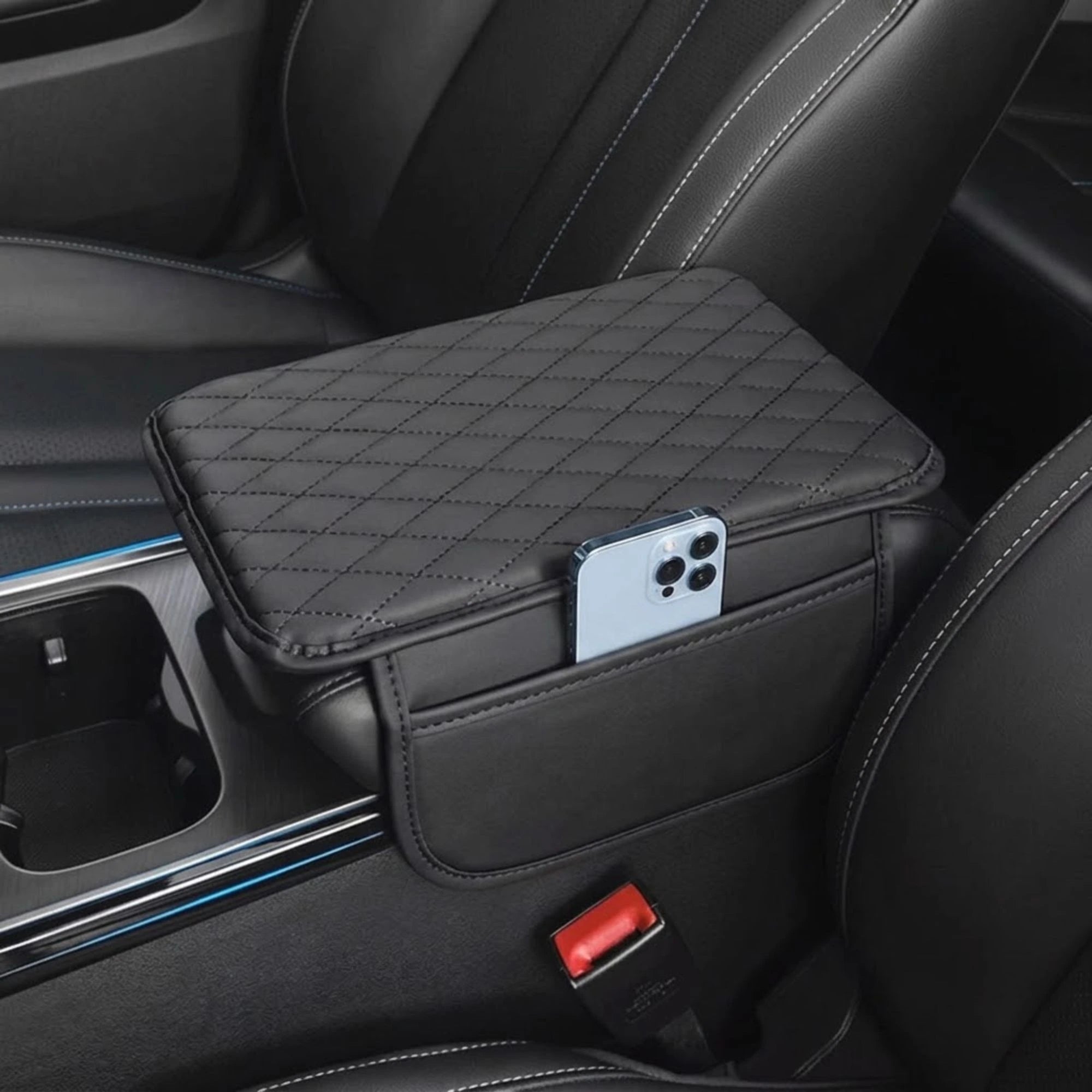 A black quilted car center console organizer tray mounted between front seats, shown holding a smartphone in its side pocket. The product is installed inside a car interior with black leather seats.