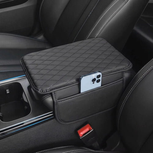 A black quilted car center console organizer tray mounted between front seats, shown holding a smartphone in its side pocket. The product is installed inside a car interior with black leather seats.