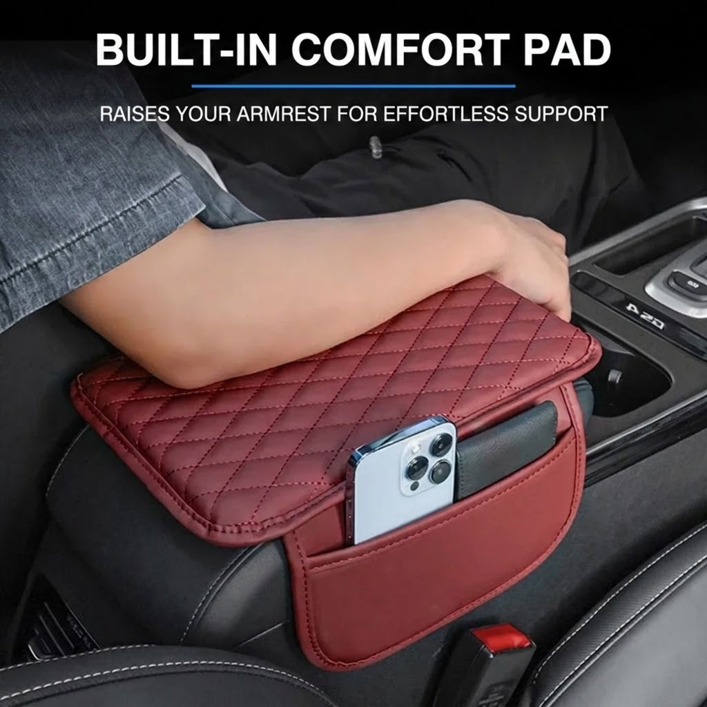 A quilted burgundy car armrest pad with a side pocket holding a phone, shown installed on a car seat with a person's arm resting on it. Text at the top reads 'BUILT-IN COMFORT PAD RAISES YOUR ARMREST FOR EFFORTLESS SUPPORT'.