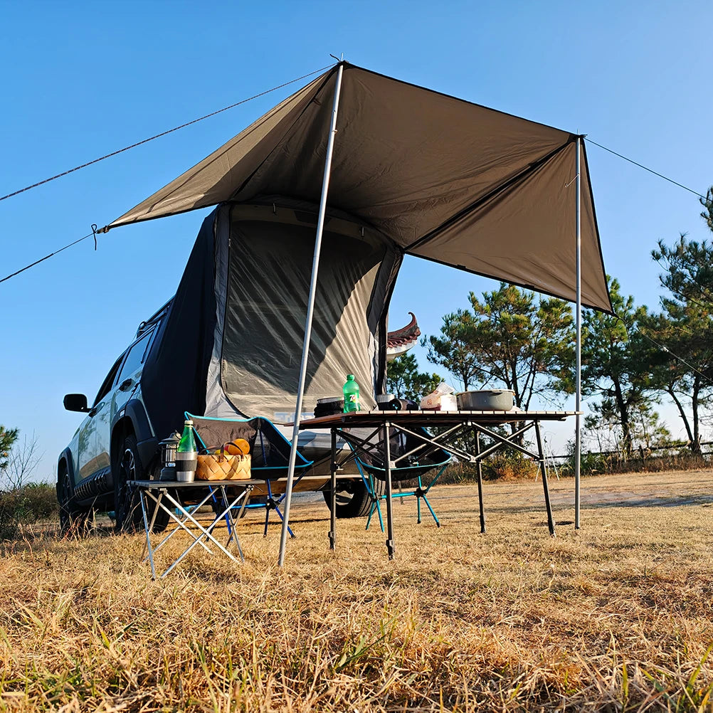 Overland Tailgate Tent with sun awning attached to an SUV on grass, sheltering a camp table and chairs in sunshine