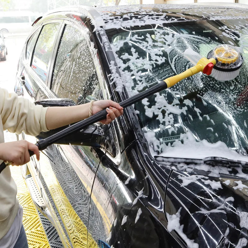 Person using the rotating foam wash mop to wash soap suds off a car windscreen and bonnet