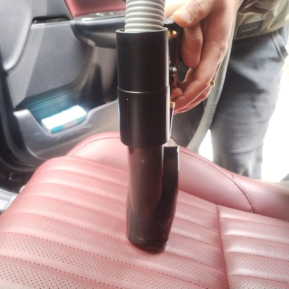 Hand using the air detailing gun's vacuum attachment to clean a red leather car seat