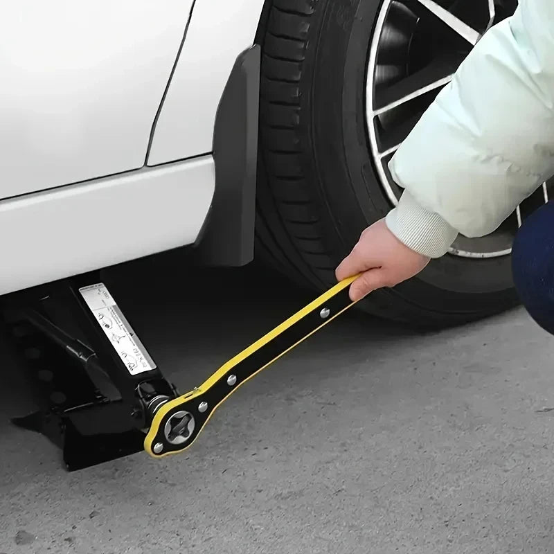 Hand using a yellow ratchet jack wrench to raise a car with a scissor jack on the roadside