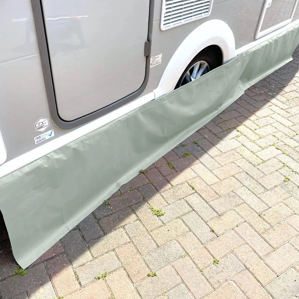 Grey Caravan Awning Draught Skirt fitted below a caravan's door and wheel arch on a brick-paved pitch