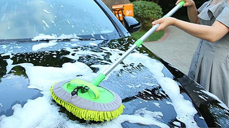 Person using a car washing brush on a black car, with a woman in a gray dress washing a car in a driveway.