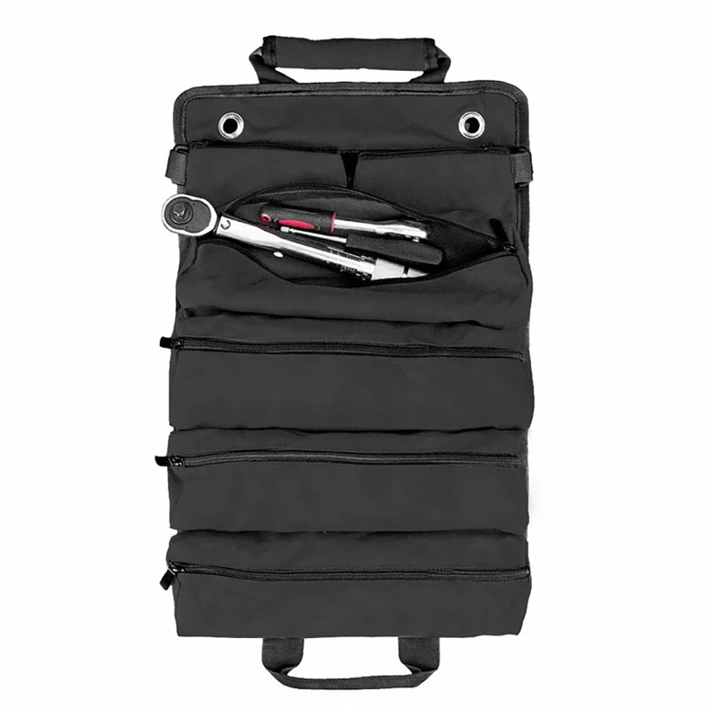 Overhead flat-lay of the black Canvas Tool Roll Organiser fully unrolled on a white background, showing grommets, carry handle and one open zip pocket with a ratchet and pliers.