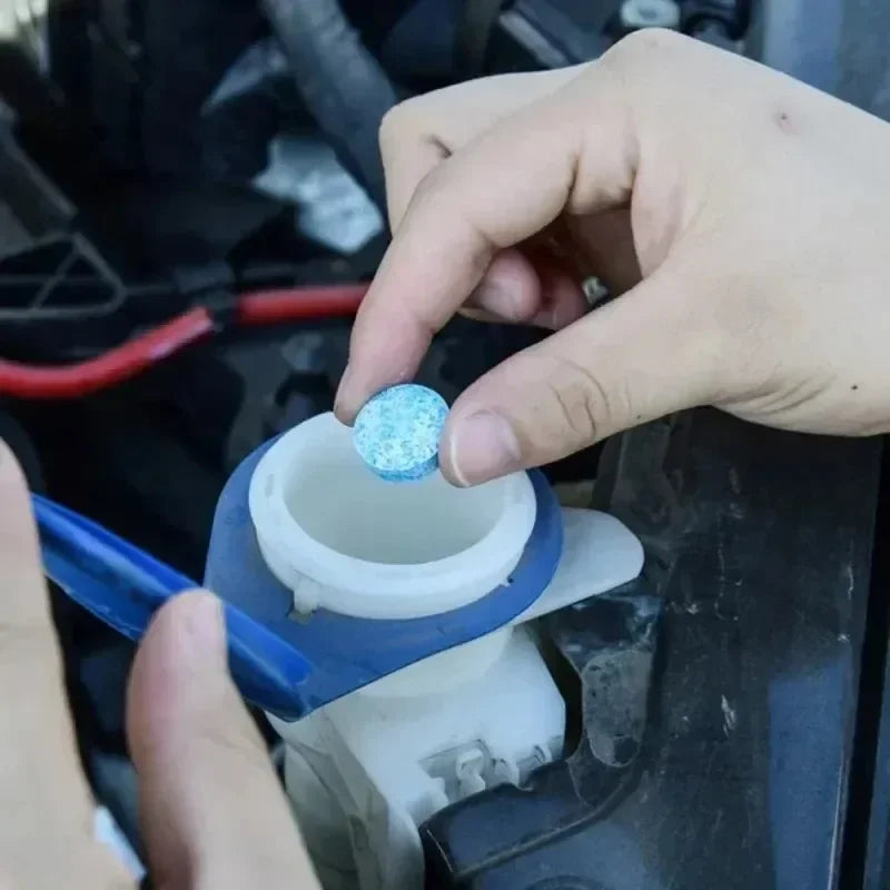 Hand placing a Windscreen Washer Fluid Tablet into a car's washer fluid reservoir under the bonnet