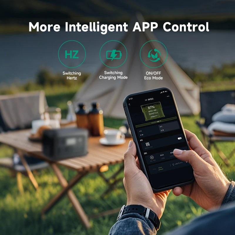 Hand holding a smartphone showing the app controls for the 600W LiFePO4 Power Station, with the unit on a campsite table behind