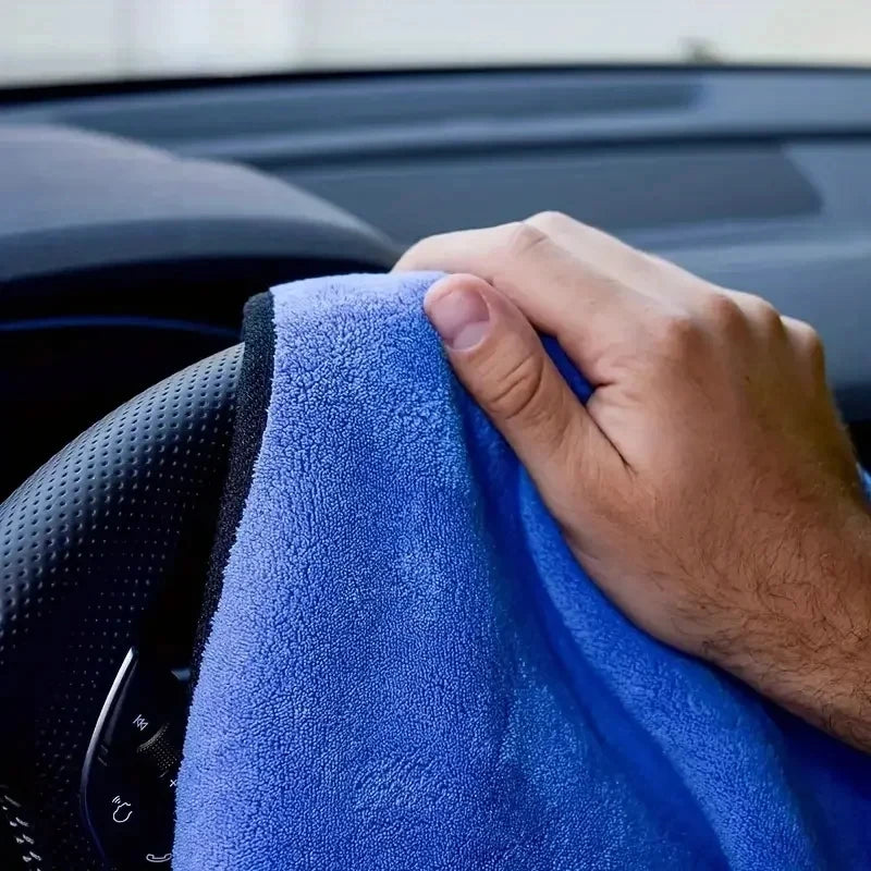 Hand using a blue microfibre car wash towel to wipe down a car's black steering wheel