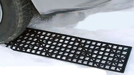 Two black rubber grid under-vehicle mats shown on a white background, with one mat demonstrated under a car tire in snow and a product box visible on the left.