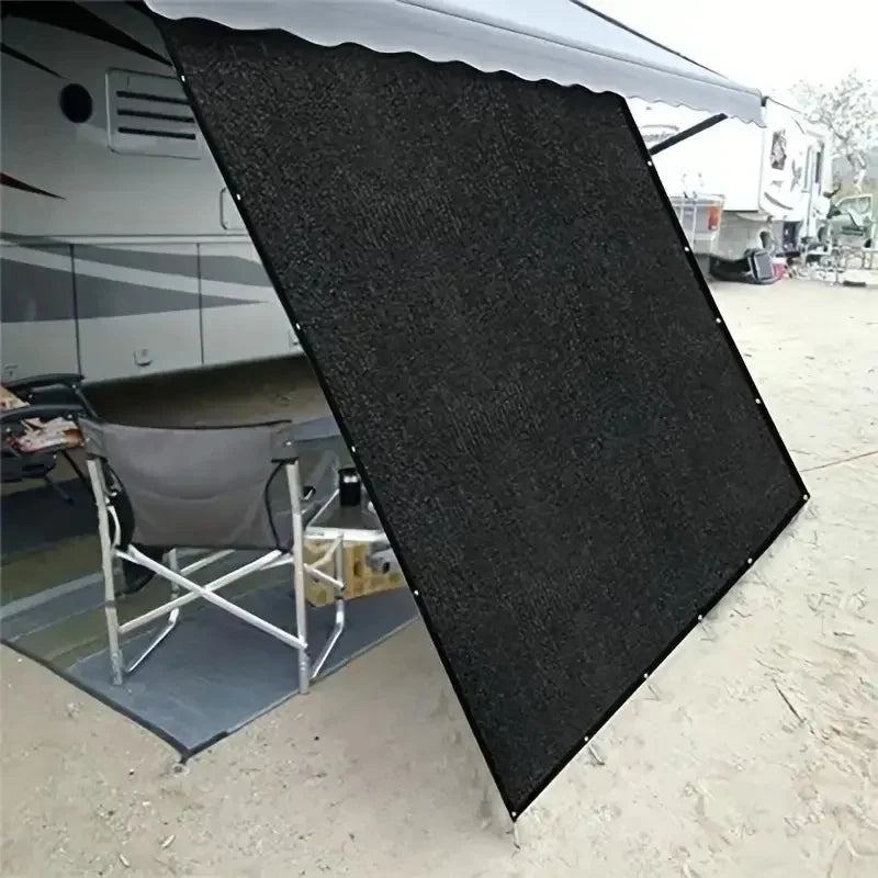 Black HDPE Sun Shade Net hanging from a caravan roll-out awning, shading camp chairs on sandy ground at a campsite
