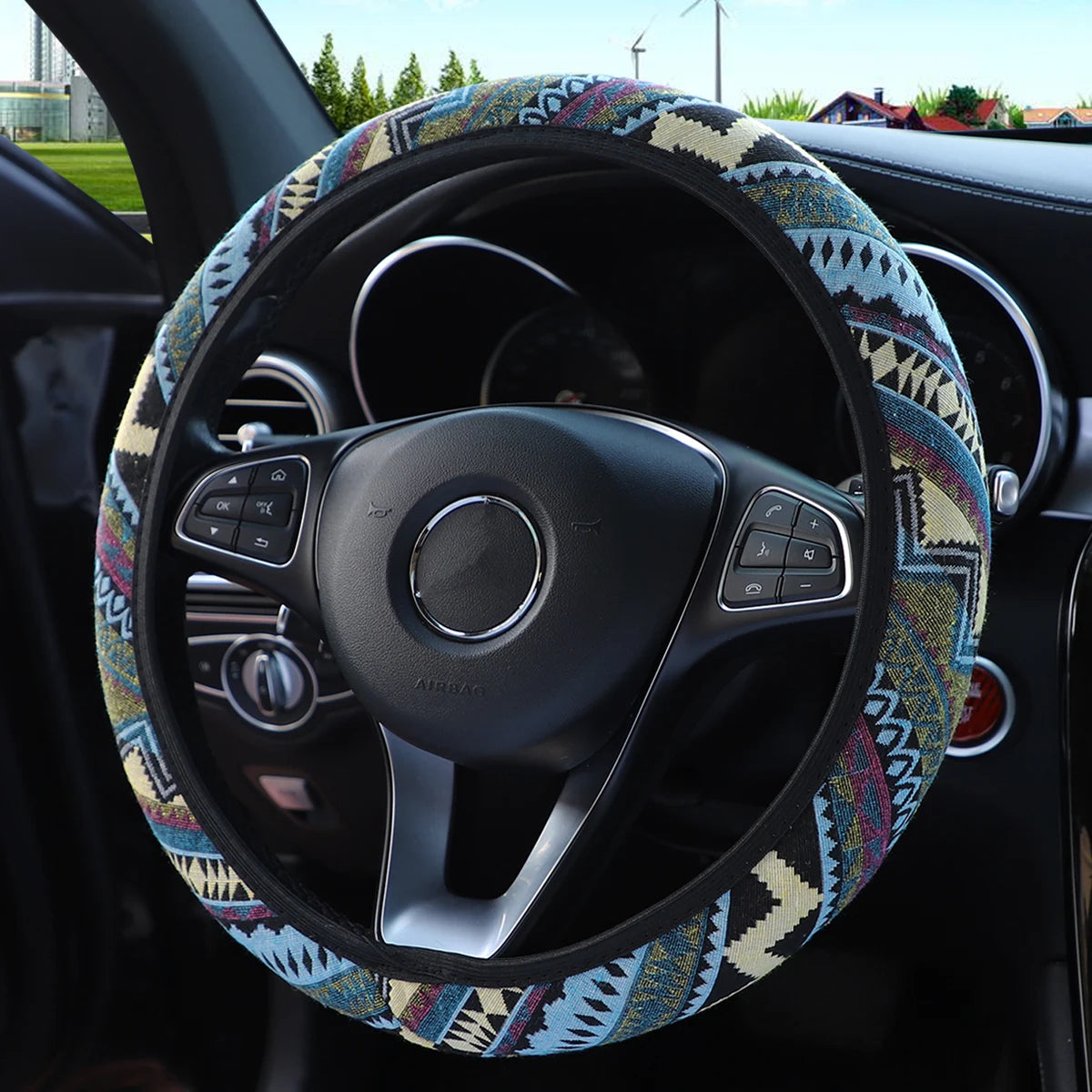 Blue, red and beige tribal pattern linen steering wheel cover fitted on a car steering wheel viewed against a suburban outdoor background