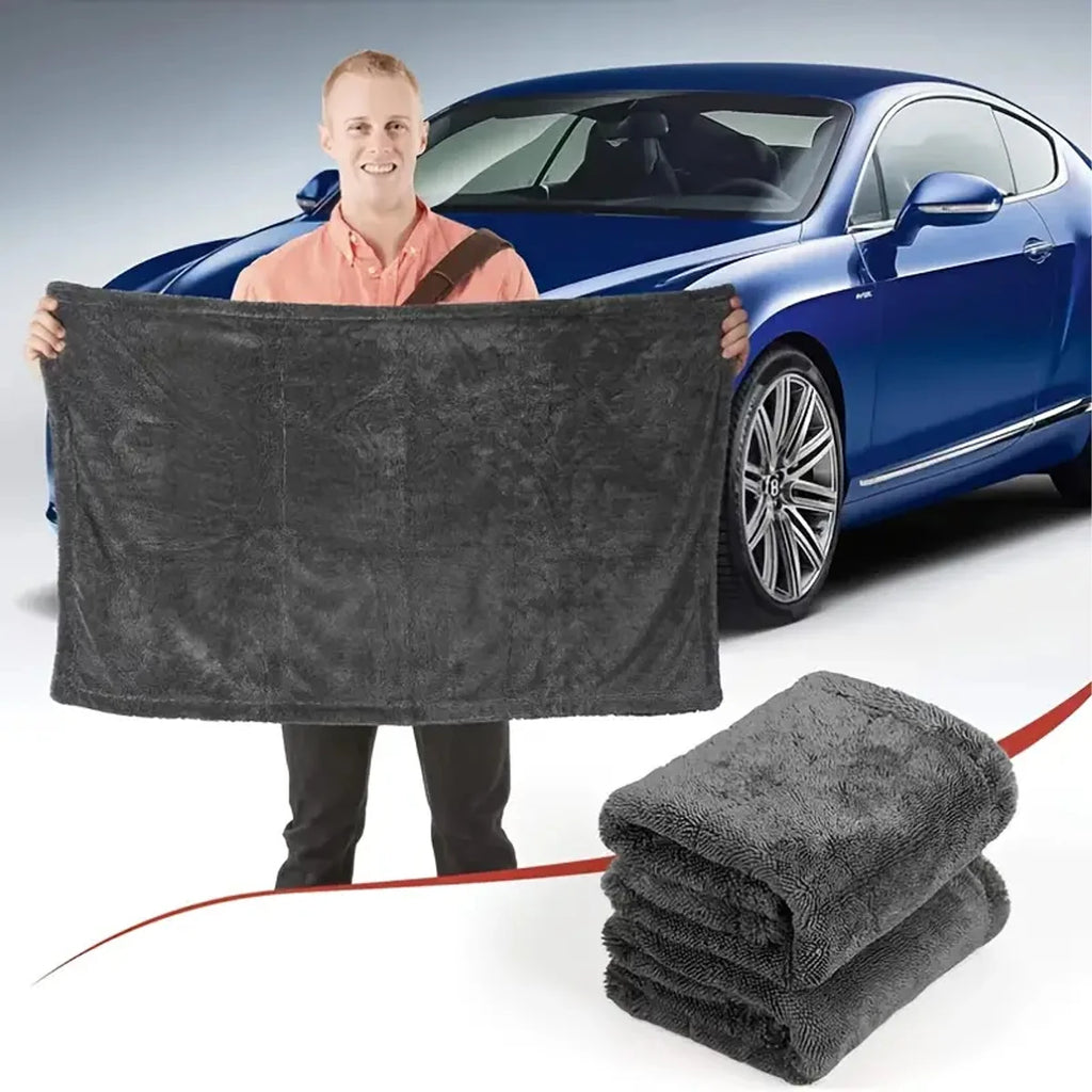 Man holding open microfibre car drying towel in front of a blue car, with a folded towel stack in the foreground