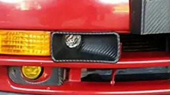 Two silver metallic flexible exhaust pipes with black carbon-fiber-look end caps, shown on a white background with two small inset photos demonstrating installation on a vehicle front grille.