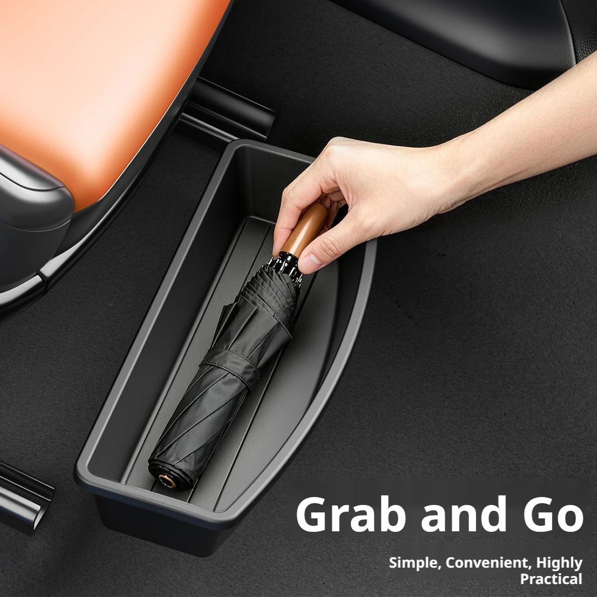 Hand placing a folded umbrella into the Under-Seat Storage Drawer beneath an orange car seat, labelled Grab and Go