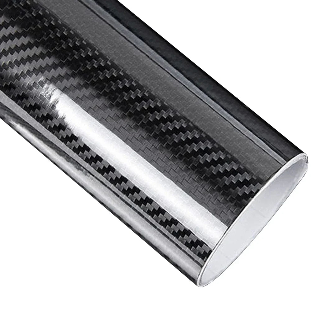 Roll of black 5D carbon fibre vinyl wrap film unrolled diagonally on a white background showing the glossy woven texture