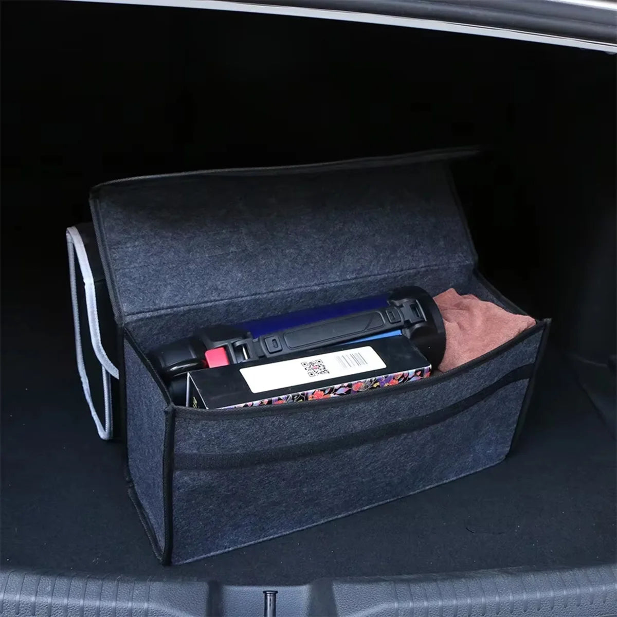 Dark grey felt storage box open in a car boot, holding tissue packs, a water bottle and other loose items to keep the boot organised.