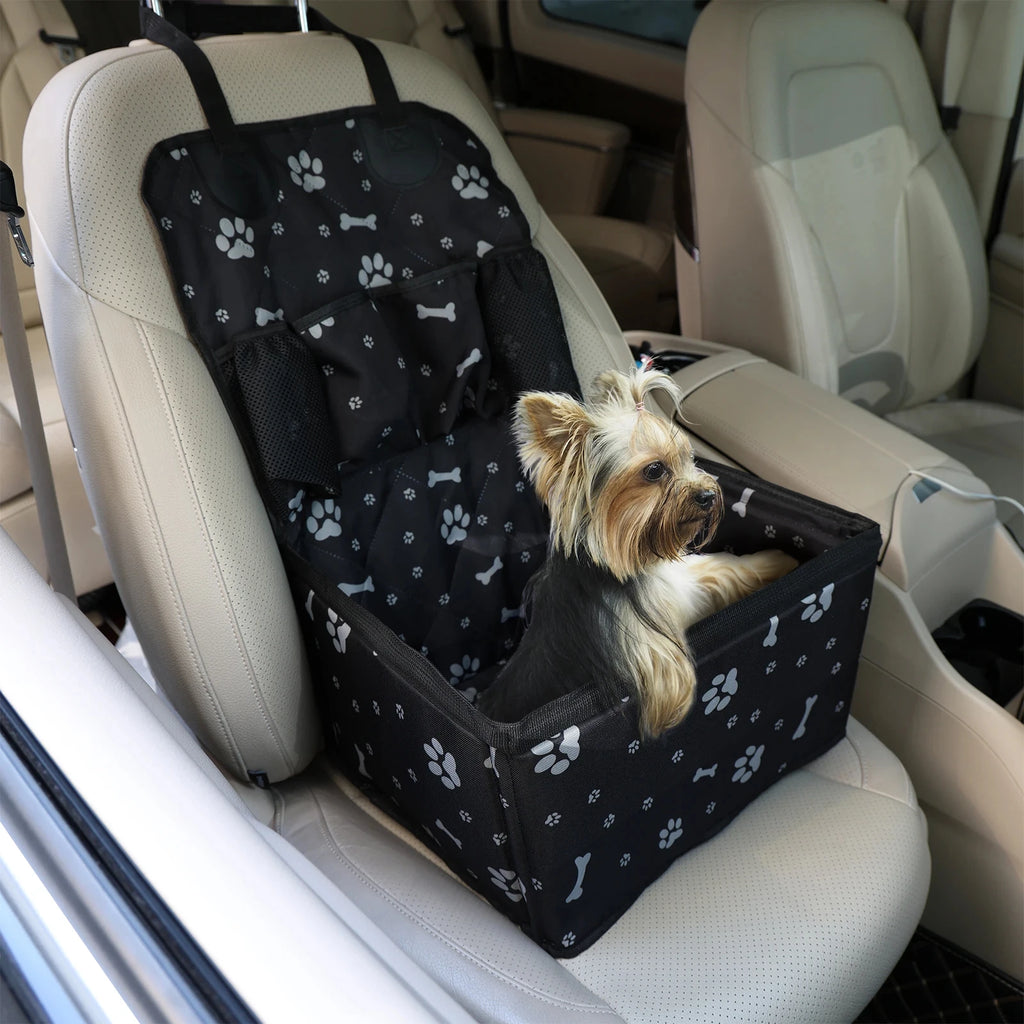 Yorkshire terrier sitting inside a black paw print waterproof dog car booster seat on a cream leather seat