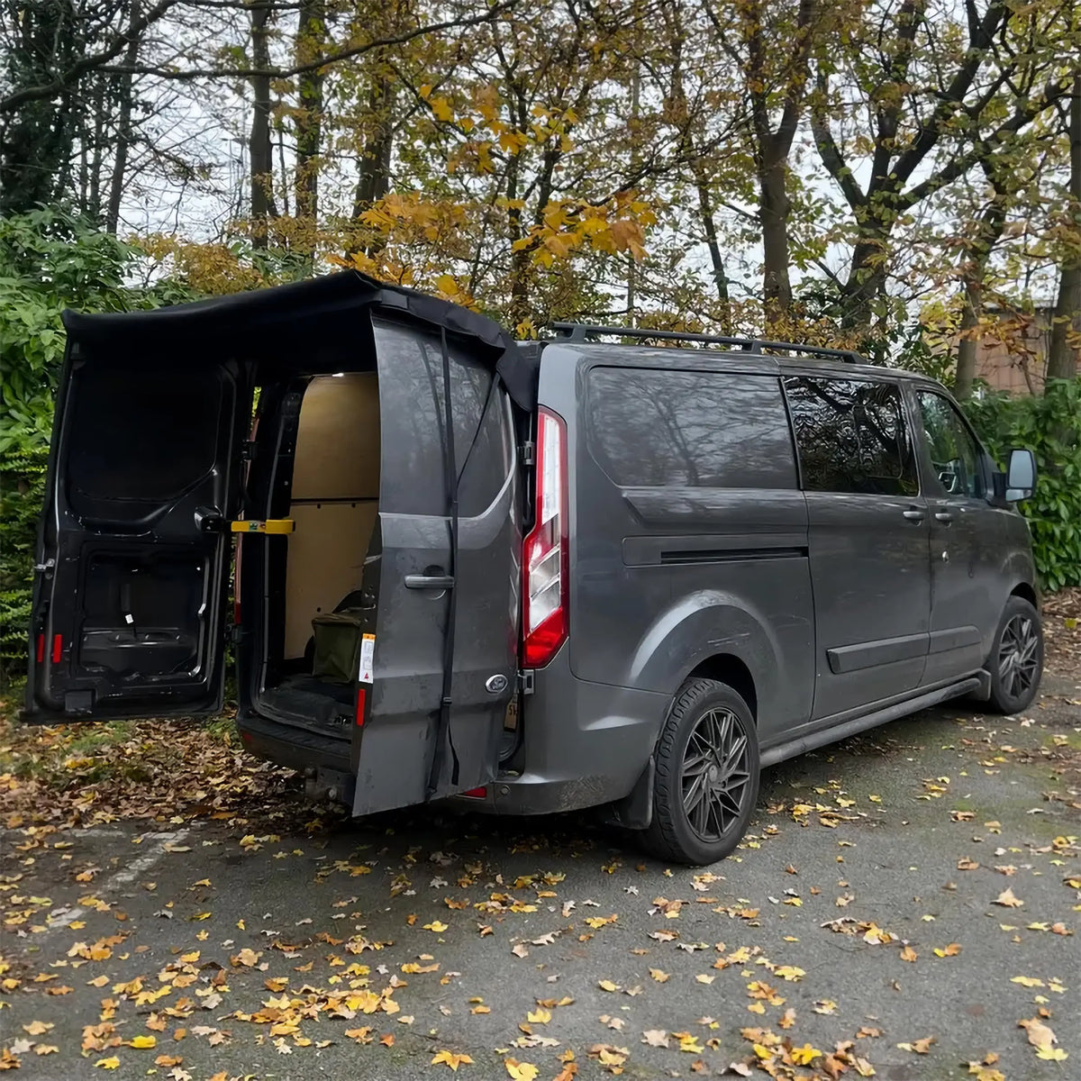 Rear Door Awning Shelter fitted over the open barn doors of a grey van, parked among autumn leaves