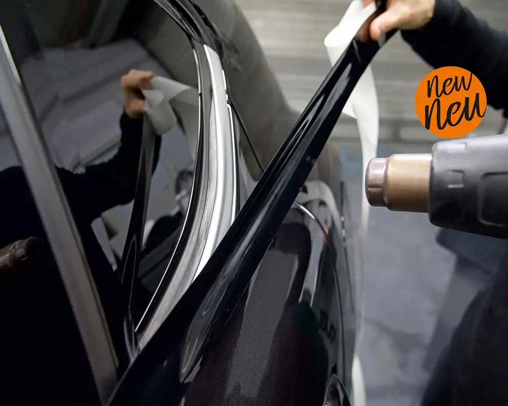 Hand using a heat gun to apply Gloss Black Trim Wrap vinyl film to a car's window trim strip