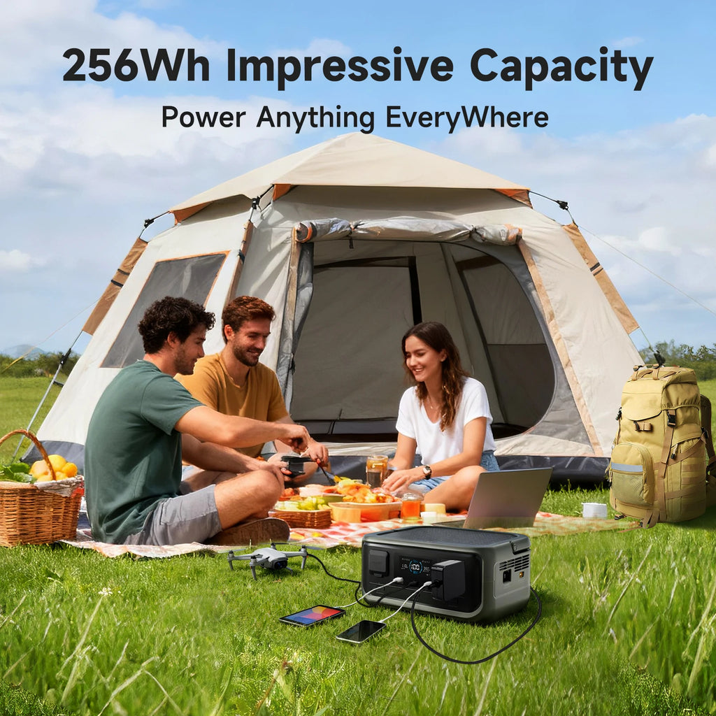 256Wh Solar Generator Kit power station charging a drone, phone and tablet on the grass beside a tent during a camping picnic