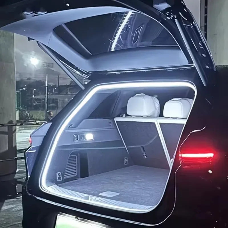 White LED trunk light strip glowing around the open boot of a car parked in a dimly lit car park at night
