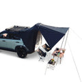 Overland Tailgate Tent attached to an SUV's open tailgate with a camp table and folding chairs set up underneath