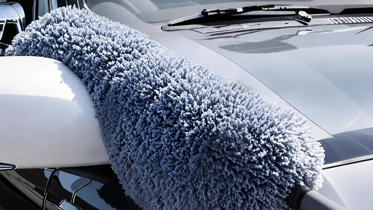 A round exterior microfiber duster with a dense blue-gray fluffy head is shown draped over a car door and hood, with large text reading 'Round Exterior Microfiber Duster' and 'Dead-Angle Dust Removal' over the windshield area.