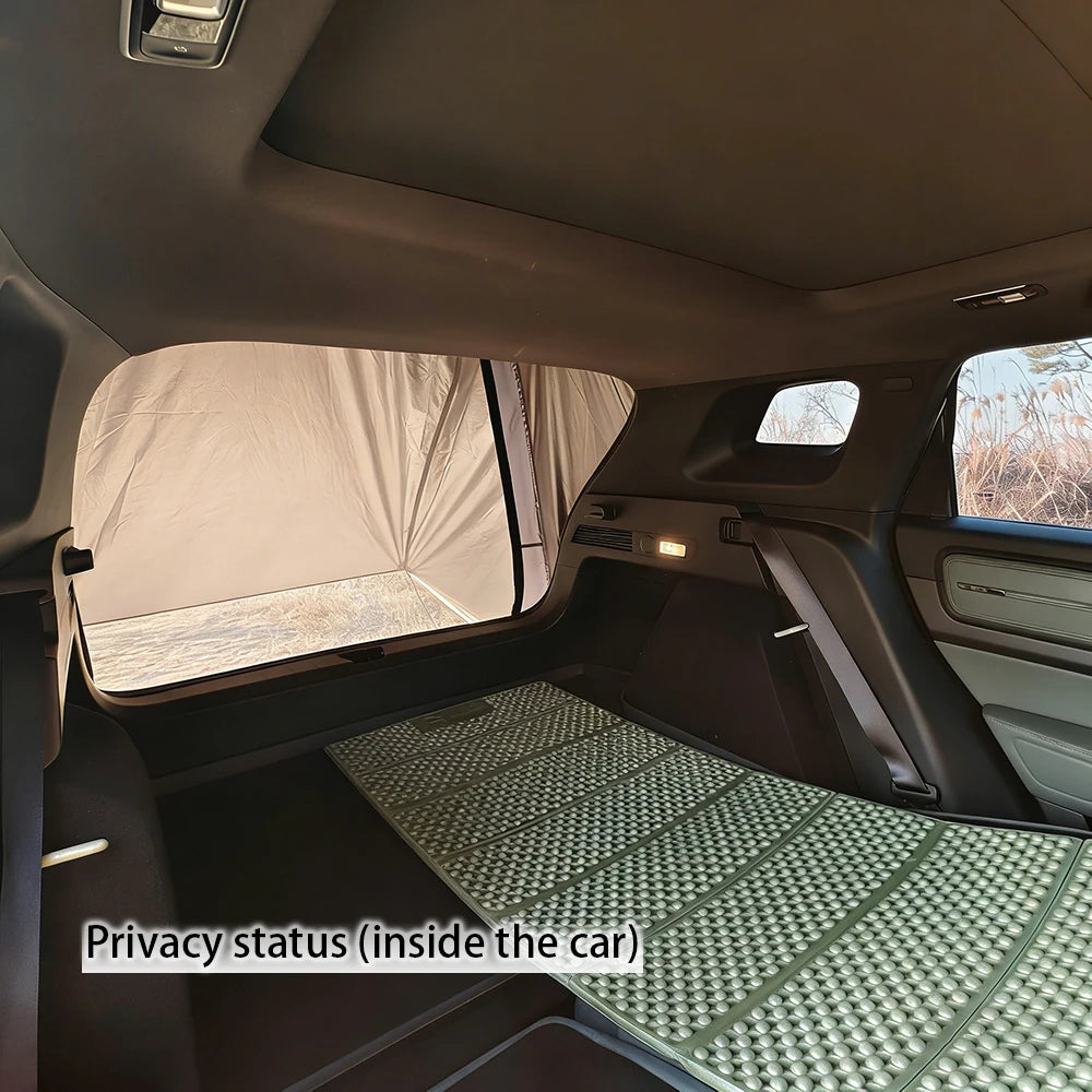 Overland Tailgate Tent privacy panel covering an SUV's rear window with a foldable sleeping mat laid out inside the car