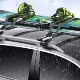 Snowboards secured on a silver car roof rack in the rain, a roof-top use for cam buckle cargo straps