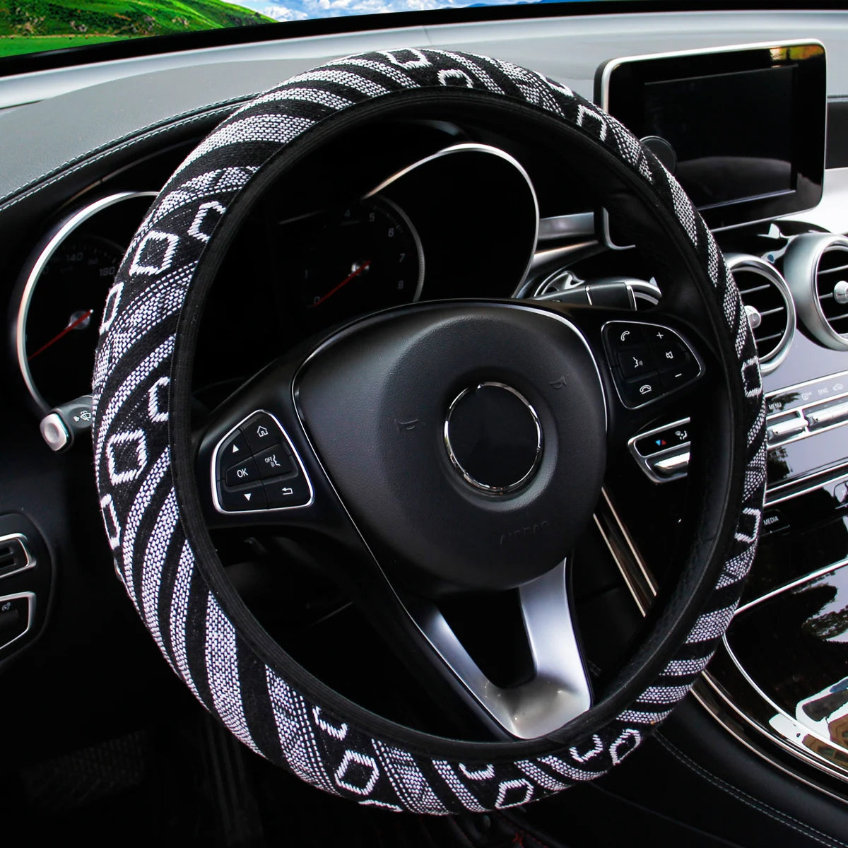 Black and white geometric pattern linen steering wheel cover fitted on a car steering wheel with dashboard visible